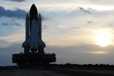 Space Shuttle Discovery moves along the crawlerway from the Vehicle Assembly Building toward Launch Pad 39A as the sun rises on a balmy Florida morning.