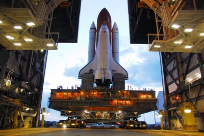 Space Shuttle Discovery, atop a mobile launch platform, moves through the doors of the Vehicle Assembly Building toward Launch Pad 39A just before sunrise on a balmy Florida morning.